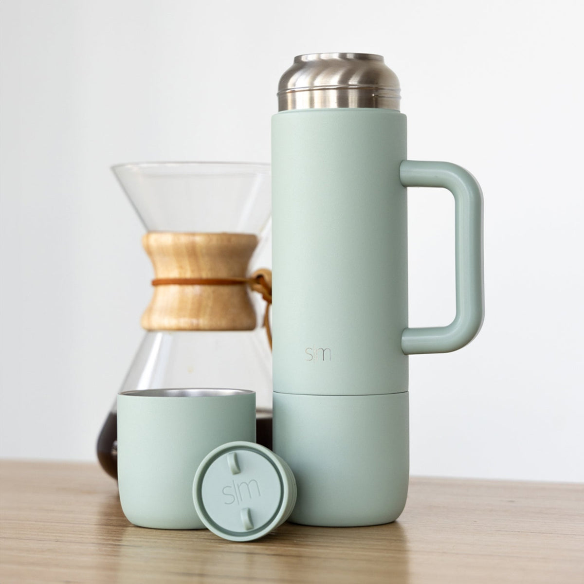 Sage green drinkware collection displayed with natural wood and stainless steel accents on a soft, neutral background